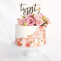 a white cake with pink flowers on top that says twenty and is decorated with gold lettering