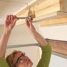 a woman is working on a beam in the ceiling above her head and holding a pair of pliers