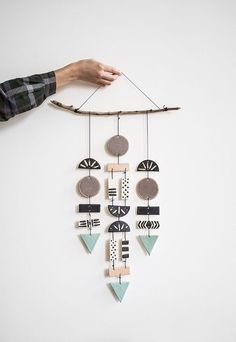 a hand holding a wooden wind chime on top of a white wall next to a stick