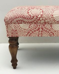 an upholstered footstool with red and white designs on the fabric, in front of a gray background