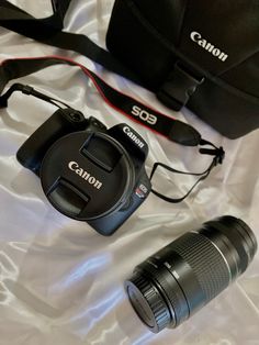 two cameras sitting on top of a bed next to a camera bag and lens cap