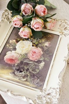 there are pink roses in a vase on the table next to an old framed photograph