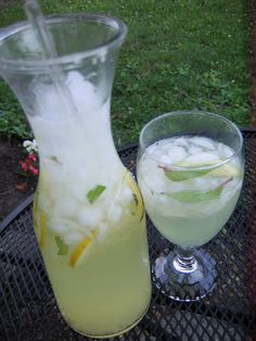 a pitcher and glass filled with liquid sitting on a metal table in front of some grass