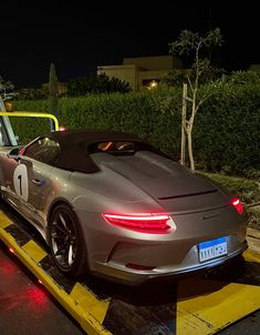 a silver sports car is being loaded onto a tow truck with its hood down and lights on