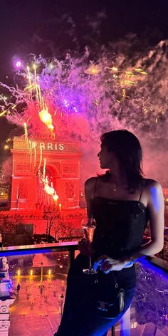 a woman sitting on top of a balcony next to a building with fireworks in the sky