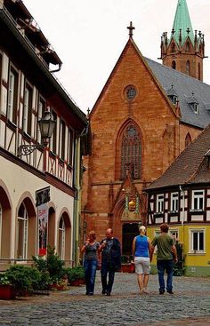 several people walking down a cobblestone street in front of old buildings with tall towers