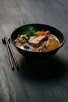 a bowl filled with meat and vegetables next to chopsticks on a wooden table