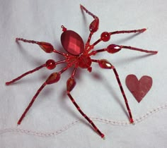 a red spider made out of glass beads on a piece of white fabric with hearts