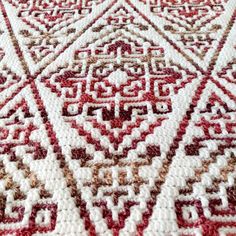 a red and white area rug with an intricate design on the bottom, in front of a wooden table