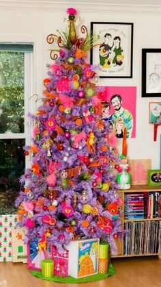 a brightly colored christmas tree in the corner of a room with pictures on the wall