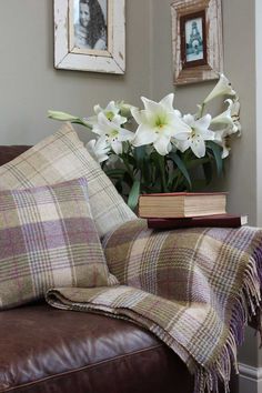 a brown leather couch with white flowers in a vase on top of it and two framed pictures above