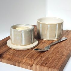 a wooden cutting board topped with two bowls and a spoon next to a bowl on top of a plate