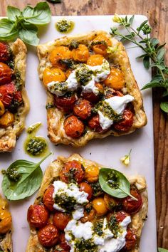 four flatbread pizzas with tomatoes, cheese and herbs on a white cutting board