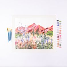 an art work with watercolors and pencils on a white surface next to some plants