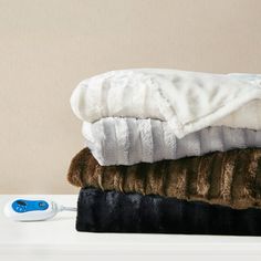 three blankets stacked on top of each other next to a hair dryer and brush