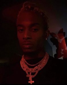 a young man wearing a red necklace and cross pendant in front of a dark background