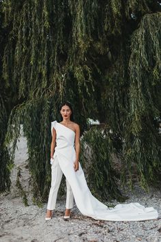 a woman standing in front of a tree wearing a white one - shoulder wedding dress