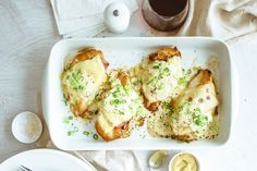 a white plate topped with chicken covered in cheese and sauces next to a cup of coffee