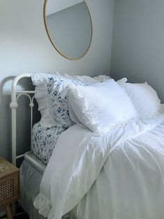 a bed with white linens and pillows in a bedroom next to a round mirror