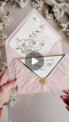 someone is opening an envelope with pink feathers and flowers on the inside, while another person holds