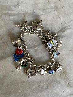 Vintage British silver charm bracelet. Made in the UK in the 1950s. This bracelet has an abundance of 22 charms:  bell, arms of Bremen, map of Wales, Eros,  enamelled flower, Welsh hat, Cornish pinkie,  Manx Isle of Man, yacht, Albert memorial,  enamelled gentian bell, Noah's Ark which opens to reveal animals, enamelled St Mary's  Rye, Highland stag, enamelled Lakeland,  silver British threepenny bit from 1917 with the  head of George V, vintage ice skates, boot,  Royal Coronation coach, clover Collectible Sterling Silver Jewelry With Vintage Charm, Sterling Silver Jewelry With Vintage Charm For Collectors, Sterling Silver Jewelry With Vintage Charm, Silver Charms Jewelry Souvenir, Silver Charm Bracelet As Souvenir, Metal Charms With Lobster Clasp For Collectors, Enamel Charms Bracelet, Silver Enamel Jewelry Souvenir, Vintage Silver Souvenir Charms