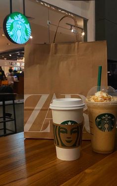 two cups of starbucks coffee sitting on top of a wooden table