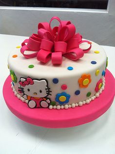 a hello kitty birthday cake on a pink plate with polka dots and a big bow