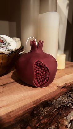 a red object sitting on top of a wooden table next to a white vase and candle