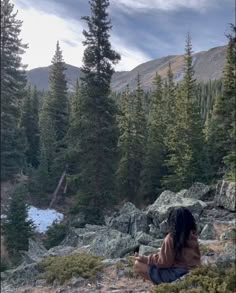 a woman sitting on top of a rocky hillside next to trees and snow covered ground