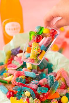 a person scooping candy into a bowl with gummy bears in it and other candies scattered around