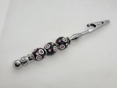 a close up of a metal object on a white surface with black and pink beads