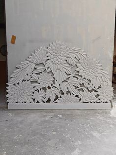 an intricately carved panel with flowers and leaves on the outside, is displayed in front of a white wall