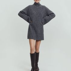 a woman in a gray sweater dress and black boots is standing with her hands on her hips