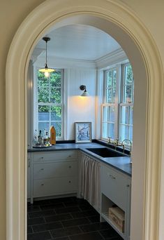 an arched doorway leads to a kitchen with white cabinets and black counter tops, along with a sink