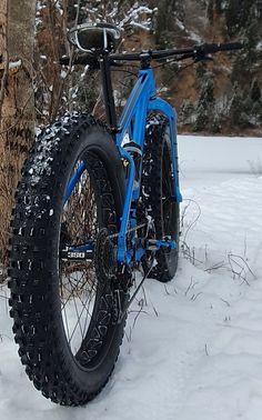 a blue bike parked in the snow next to a tree