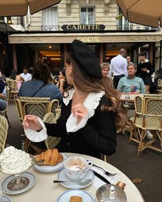 a woman sitting at a table with food and drinks in front of her on the street