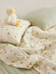 a teddy bear sitting on top of a bed covered in white sheets and yellow flowers