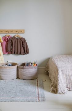 two baskets with clothes hanging on the wall next to a bed and rug in a bedroom