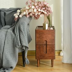 a wooden nightstand with flowers on it next to a blanket