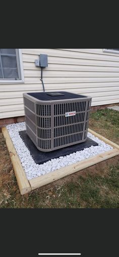 an air conditioner sitting on top of gravel in front of a house with grass and rocks around it