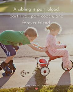 two children on tricycles playing with each other in the street and one is pushing another child's hand