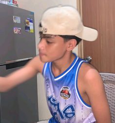 a young man wearing a white hat sitting in front of a refrigerator with magnets on it