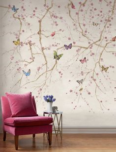 a pink chair sitting in front of a wall with flowers and butterflies painted on it