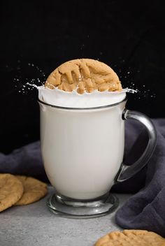 a cookie being sprinkled into a cup of milk with cookies around it on the side