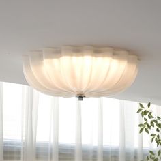 the light fixture is hanging from the ceiling in front of sheer curtained windows with white drapes