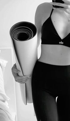 a woman holding a yoga mat in her right hand and wearing a sports bra top