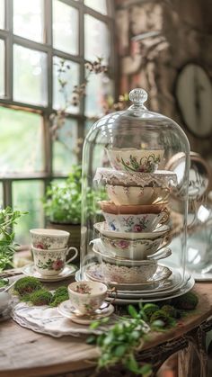 a glass clochet filled with cups and saucers on top of a wooden table