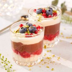 two desserts with berries and other toppings in small glass dishes on a table