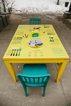 a yellow and blue table with chairs on it in the middle of a sidewalk next to snow covered ground