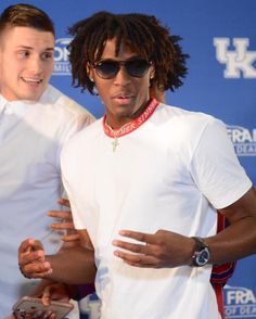 two young men standing next to each other in front of a blue wall wearing sunglasses